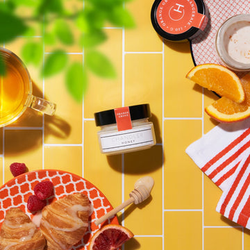 Orange Grove Honey (Chandler Honey) - Small jar of handmade Canadian Orange Grove Honey with honey dipper and croissants on yellow tile background.