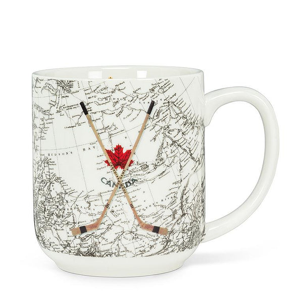 A white mug with a black and white navigational map of Canada. On top, there is a red maple leaf and two wooden hockey sticks crossed over each other.