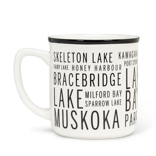 White mug with a black rim, a red canoe oar, and black text listing names of Muskoka lakes.