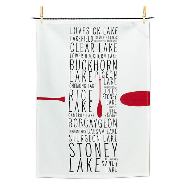 White tea towel with black text down the middle listing Kawartha lake names with a red canoe oar.