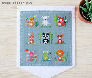 A blue fabric square with 9 different animals cross-stitched on it, stitched to a white banner