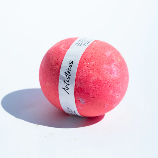 A pink, round bath bomb with a white band around it reading 