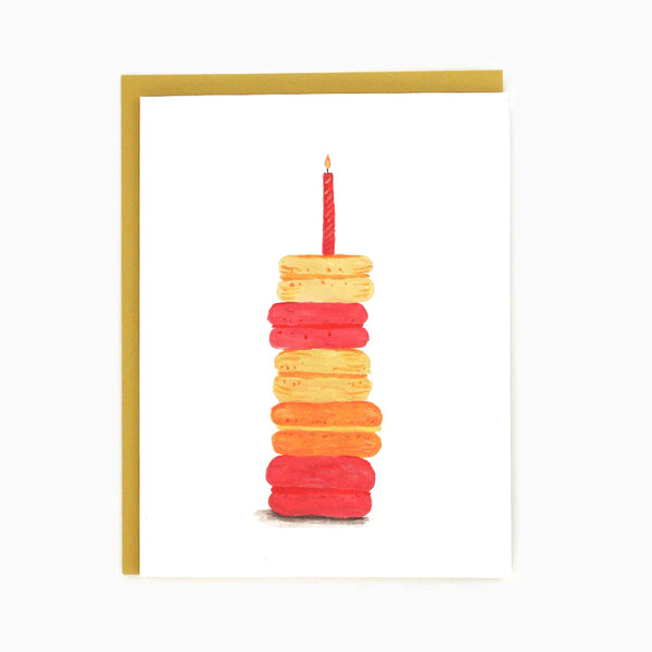 A white card with 5 macaroons stacked up with a candle