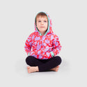 Child sitting cross-legged, wearing red hoodie with purple splotches and blue cuffs