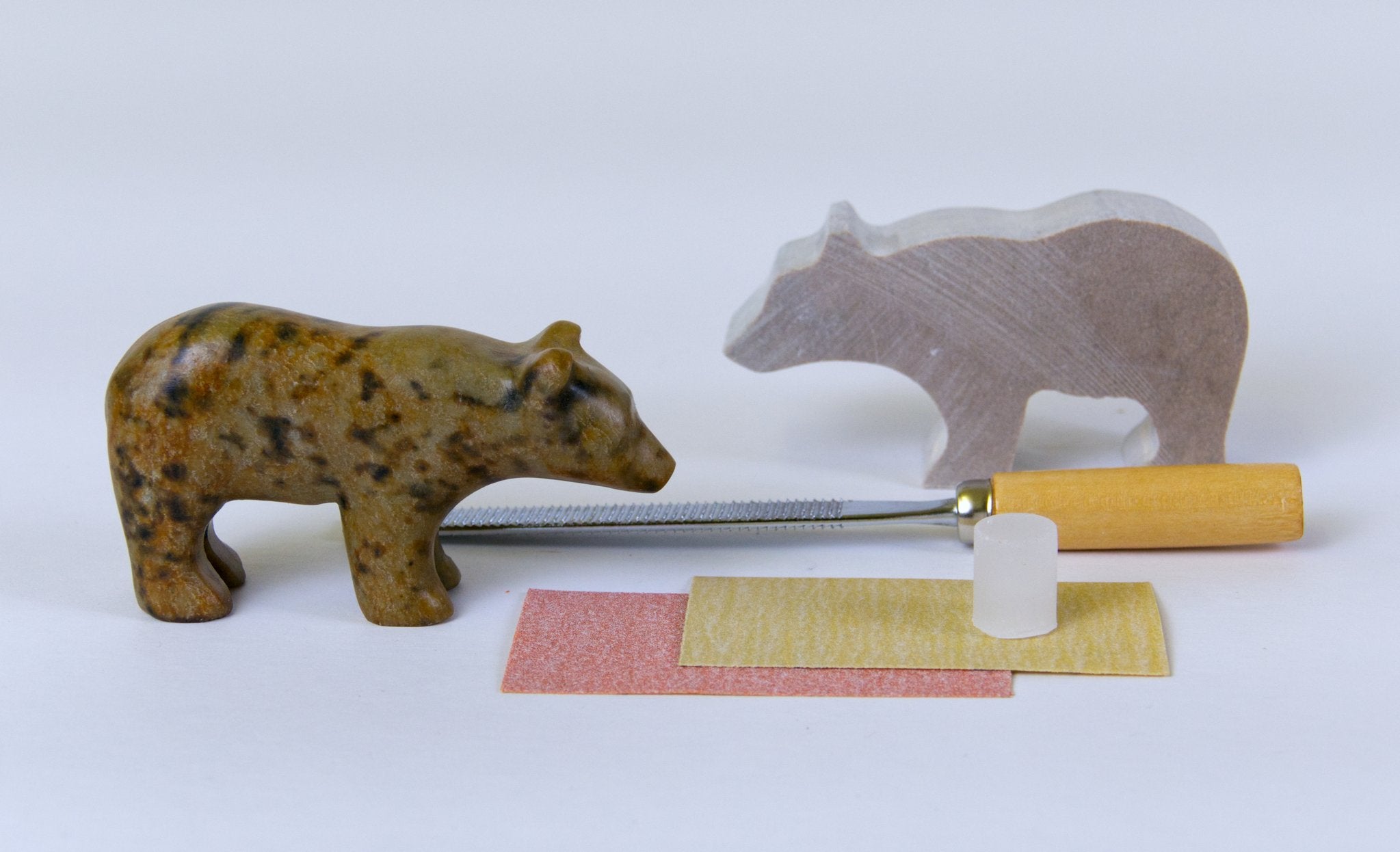 The finished bear statue next to the contents of the kit including the sanding tool and the soapstone bear before carving