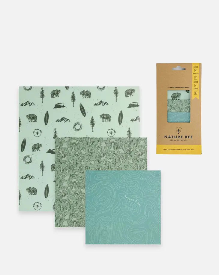 3 different sized beeswax wraps, one with a bear and tree pattern on a blue background, one with mushrooms on a blue background, and one with swirl designs on a blue background