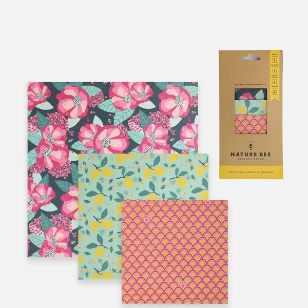 3 different sized beeswax wraps, one with pink flowers on a dark background, one with lemons on a branch on a teal background, and a pink one with line designs