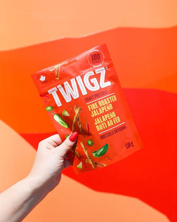 Twigz Pretzel Sticks - Fire Roasted Jalapeno - Hand holding red bag of Twigz fire roasted jalapeno pretzel sticks, unique Canadian handmade gift.