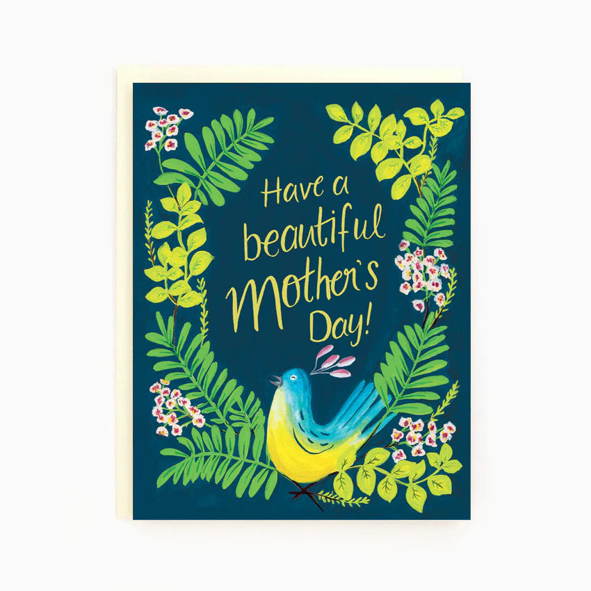 A navy blue card with illustrated leaves and small pink flowers surrounding the message in the center "Have a beautiful Mother's Day!" written in yellow. Beneath there is a blue and yellow bird