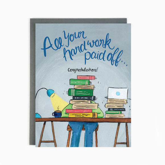 A blue card with a person studying at a desk filled with books and the words "All your hard work paid of...Congratulations!"