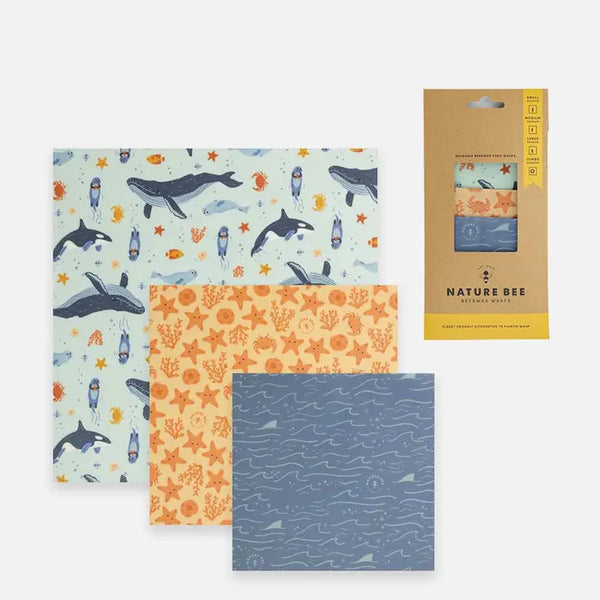 3 different sized beeswax wraps, one with whales and fish on a blue background, one with starfish and sea coral on an orange background, and a blue one with wave and shark fin design