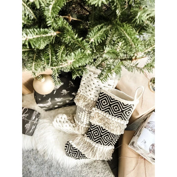 Geometric Boho Stockings | Bohemian Christmas - Black and white knitted Christmas stocking with geometric boho patterns hanging by a green pine tree.