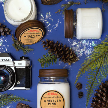 Whistler Pine Soy Candle - 14oz - Whistler Pine soy candle in a clear glass jar with wooden lid, surrounded by pinecones and evergreen branches, handmade.