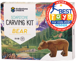 A box with a picture of a brown bear statue in front of an illustrated lake and forest. In the top right corner is a red stamp reading 