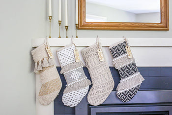 Geometric Boho Stockings | Bohemian Christmas - Four handmade Canadian boho Christmas stockings in neutral shades with geometric patterns and tassel accents hanging on a.