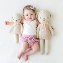A baby in between 2 different sized lamb stuffies