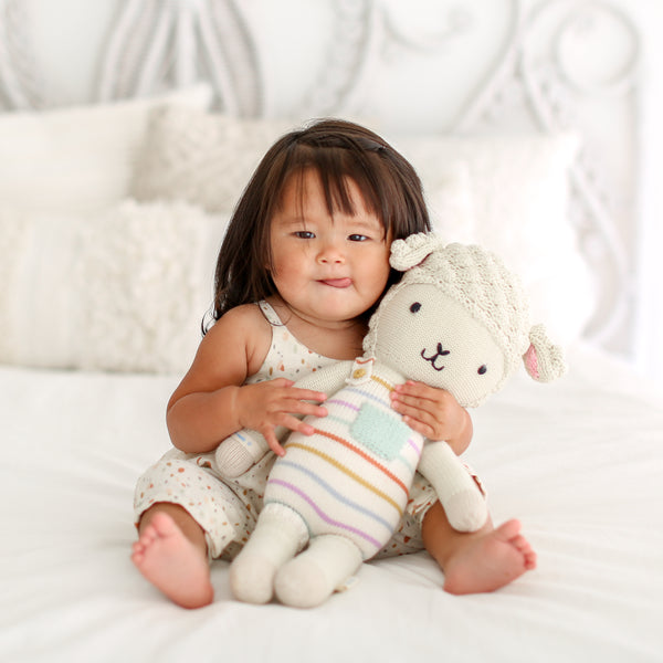 A young girl sits on a white bed holding the doll