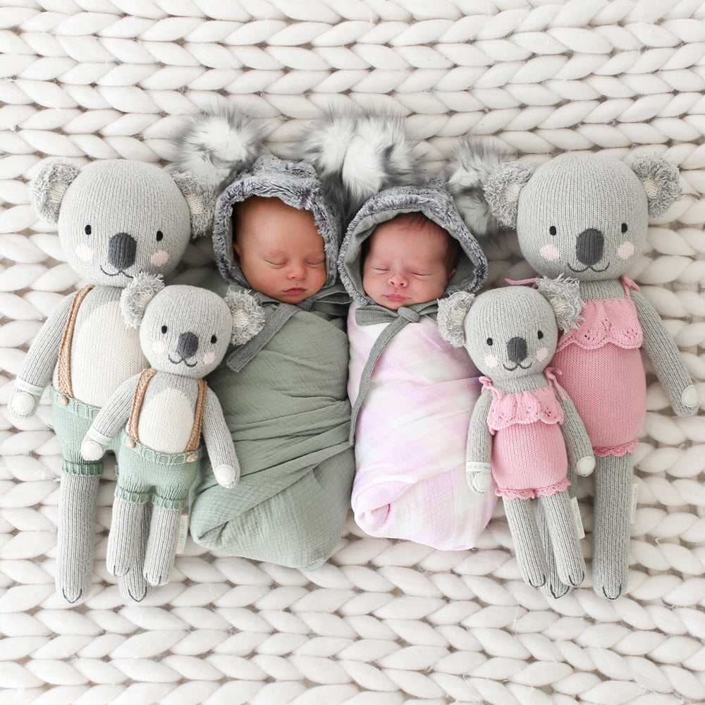 2 big and 2 smaller koalas on either side of 2 sleeping babies 