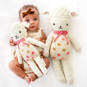 A baby holding the small lamb stuffy with the big lamb stuffy beside her