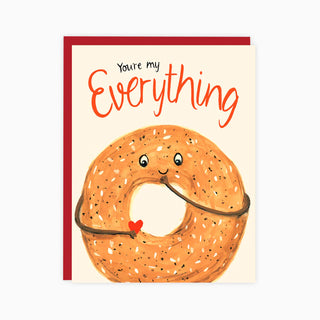 A white card with an everything bagel on it and the words 